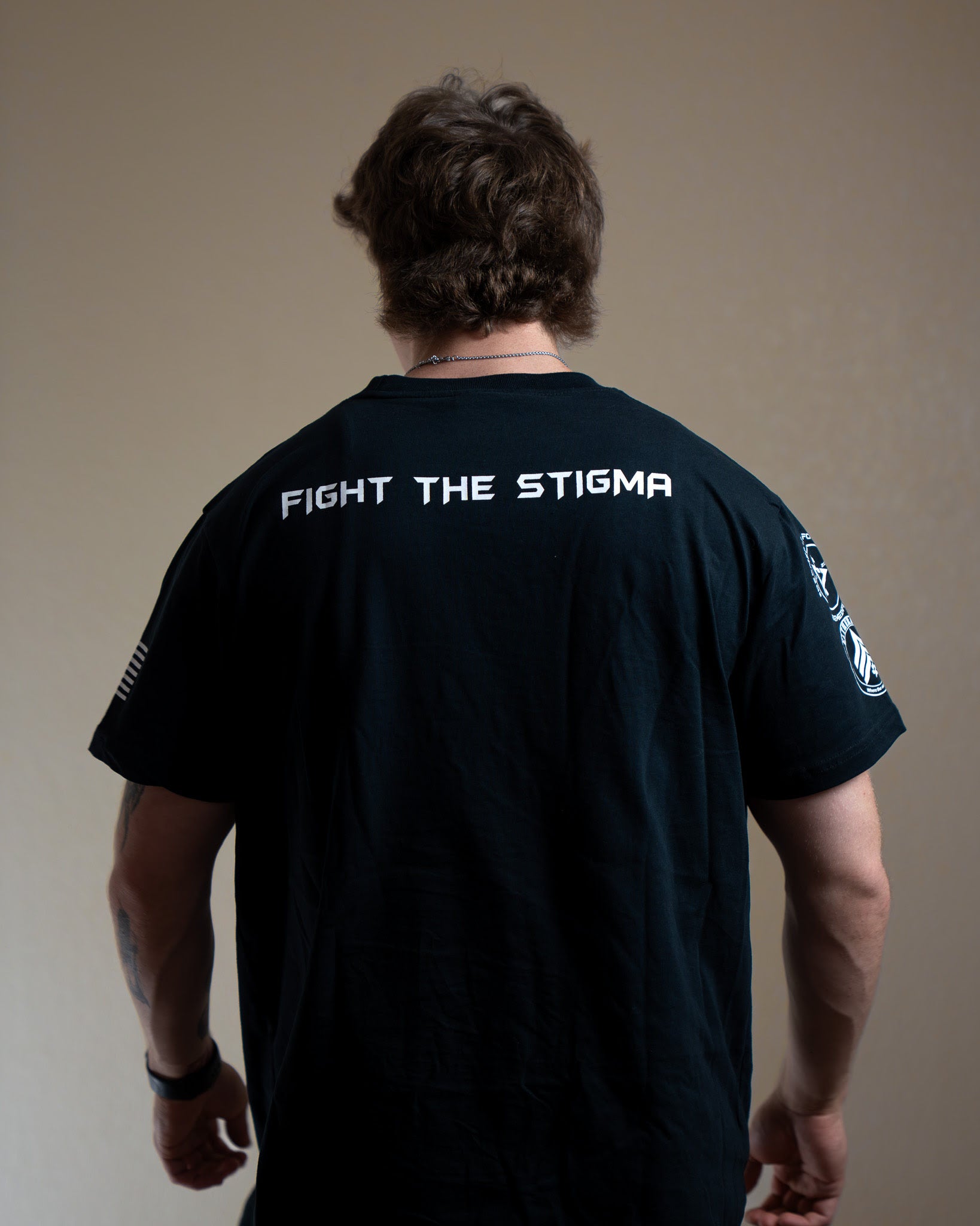 Person wearing a black t-shirt with 'Fight The Stigma' text on the back against a plain background